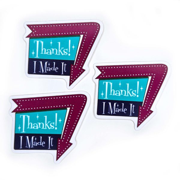 three stickers that say "Thanks! I Made It" in a 1960 sign style with arrow around one edge pointing down. Arrow is a warm purple, and the sign is aqua and dark blue with white writing