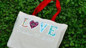 white tote bag with red handle with letters LOVE with the O as a heart from pink fabric