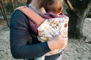 Muted flowered baby carrier with brown haired child. Parent is standing in a field