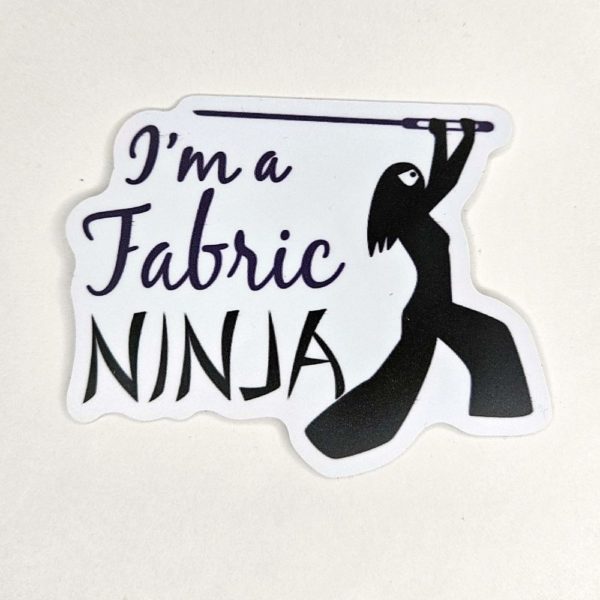 Sticker with I'm a fabric Ninja written next to a ninja outline of a woman with long hair , white mask, and wielding a large sewing needle.