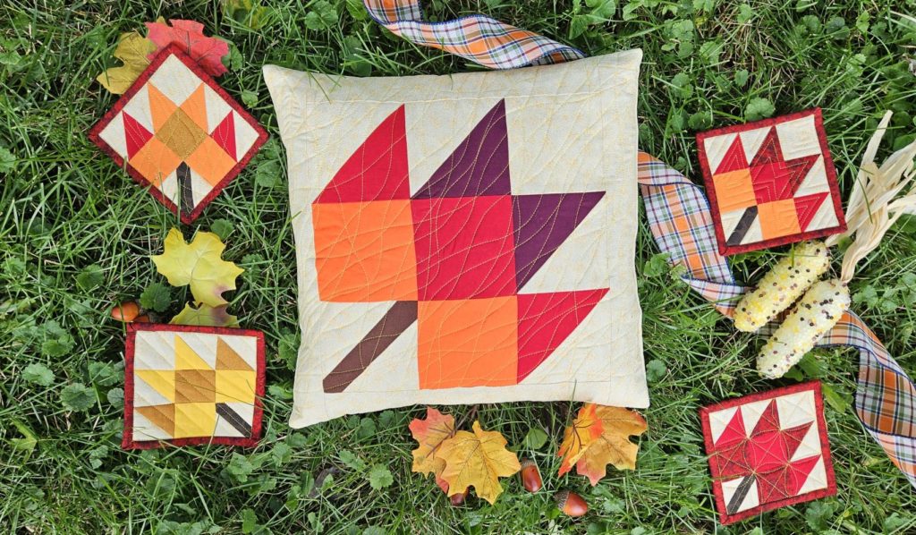 maple leaf quilted pillow in the grass surrounded by smaller maple leaf quilted coasters