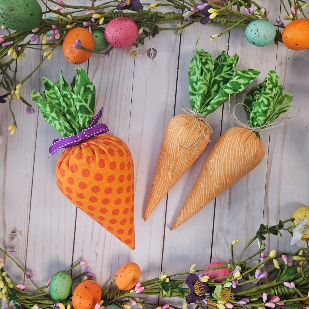 3 orange fabric carrots surrounded by a garland of leaves flowers and colorful eggs. 
