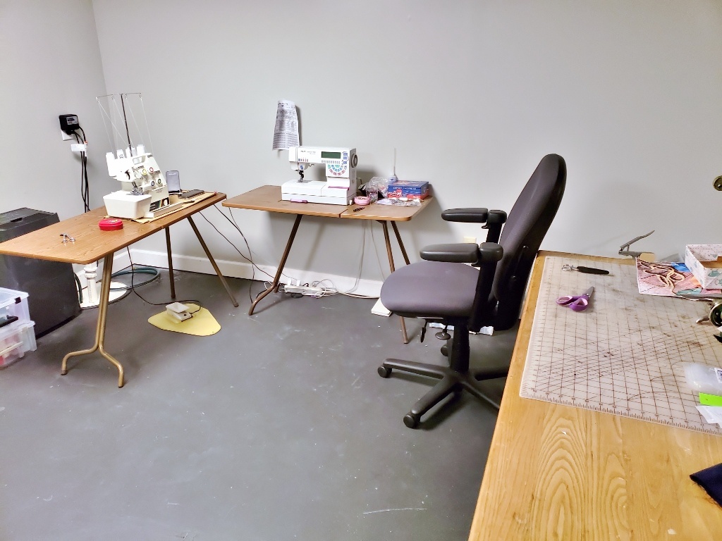 Sewing machine, serger, and work table set up in a U shape with an office rolling chair to move between them. 