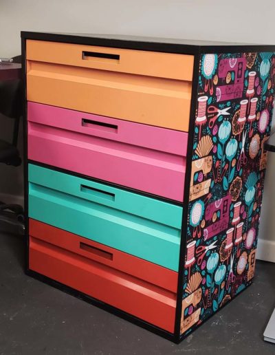 Sewing pattern cabinet that has been refurbished to have colorful drawers and sewing themed wall paper on the sides.