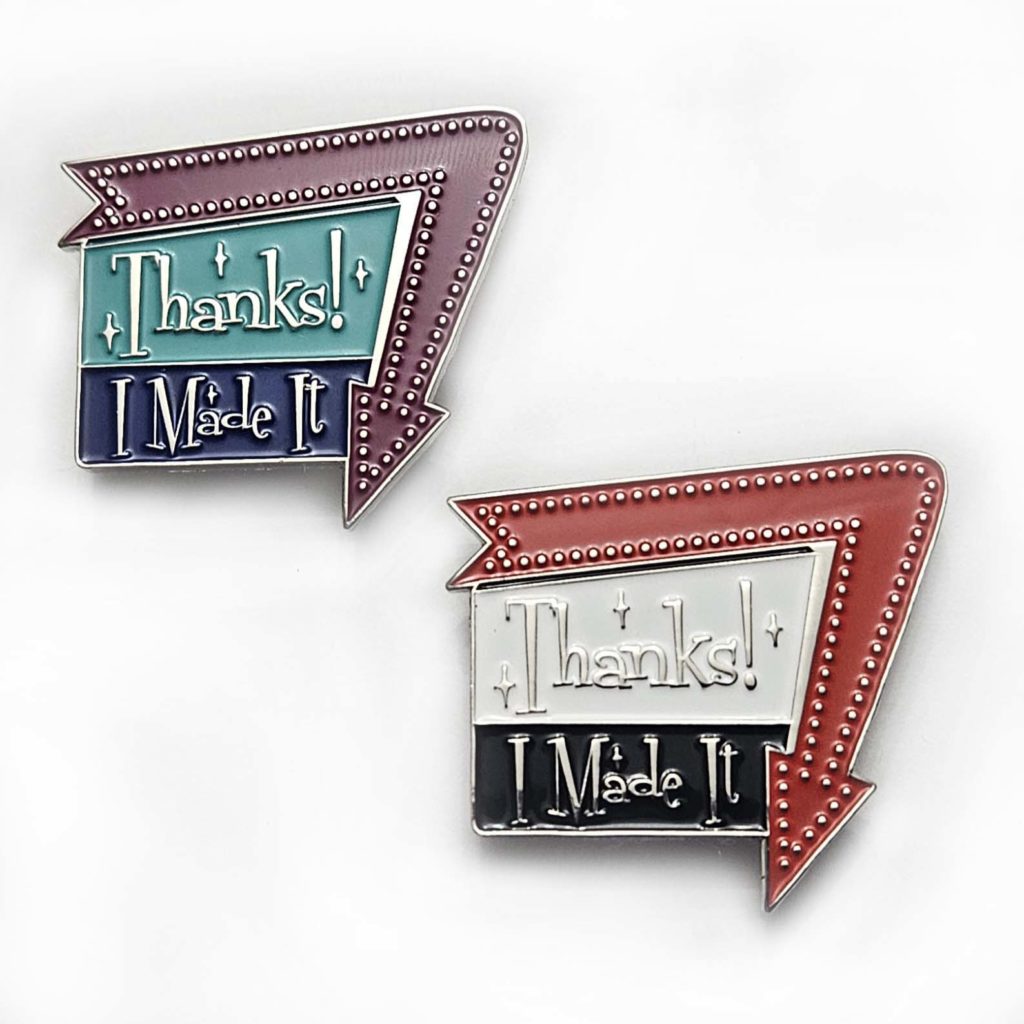 Enamel pins that say, "Thanks! I Made It" in a 1960 sign style with arrow around one edge pointing downward. Two different colors with silver metal