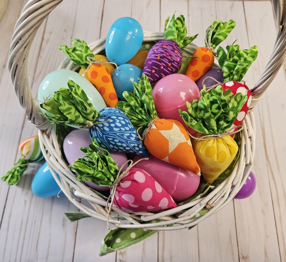white wicker Easter basket filled with pastel plastic eggs and rainbow colored fabric carrots.