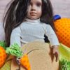 doll with dark skin and hair wearing a white turtle neck sweater has a hat in her lap and is holding a fabric carrot