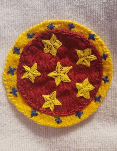 Embroidered Nova badge - red circle base with yellow ring around it. Blue stars in the yellow ring and 6 red stars in the red area.