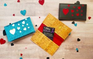 3 small wallets one red with tan hearts which is open to show the card pockets. One is blue glitter with white hearts, and one is black with red hearts.