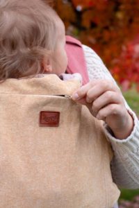 white hand opens the zipper on a cream tan slipcover on an onbuhimo carrier.