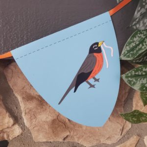 Blue dragonscale bunting flag with paper robin shape on it. Hung on an orange ribbon