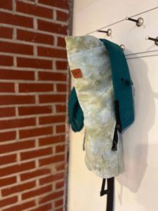 green tie-dyed slipcover on a teal happy baby carrier hanging up on a peg