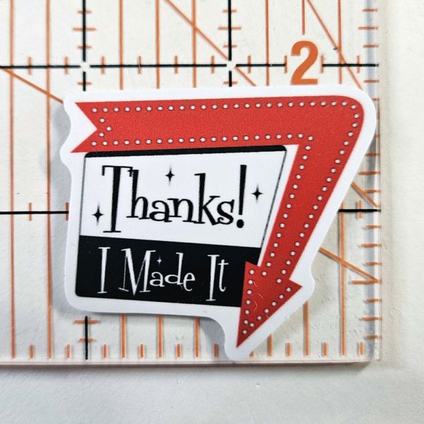 Sticker says, "Thanks! I Made It" in a 1960 sign style with arrow around one edge pointing down. Arrow is red and the sign is black and white with black writing