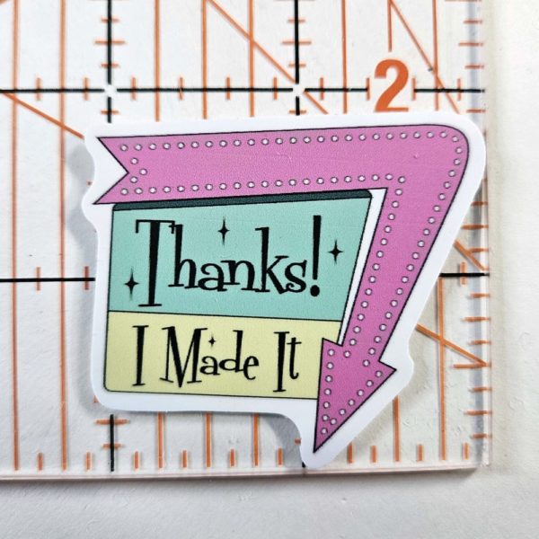 Sticker says, "Thanks! I Made It" in a 1960 sign style with arrow around one edge pointing down. Arrow is pink and the sign is Aqua and a yellow green with black writing
