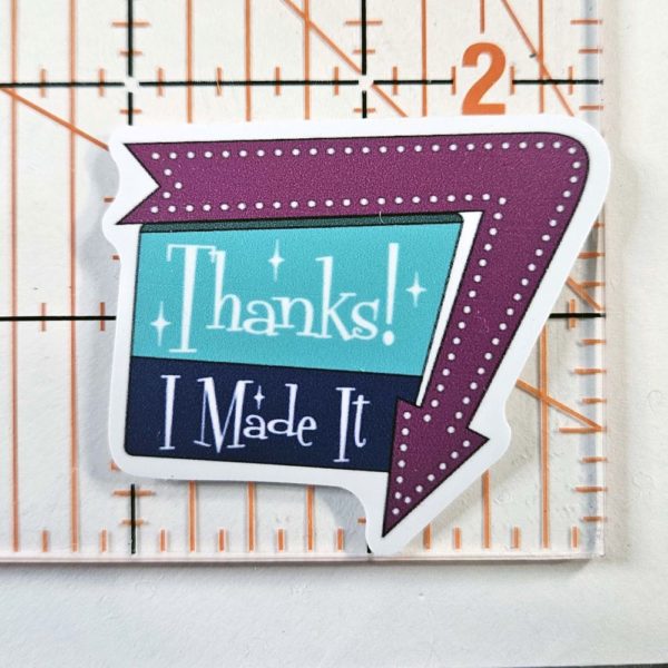 sticker that says "Thanks! I Made It" in a 1960 sign style with arrow around one edge pointing down. Arrow is a warm purple, and the sign is aqua and dark blue with white writing