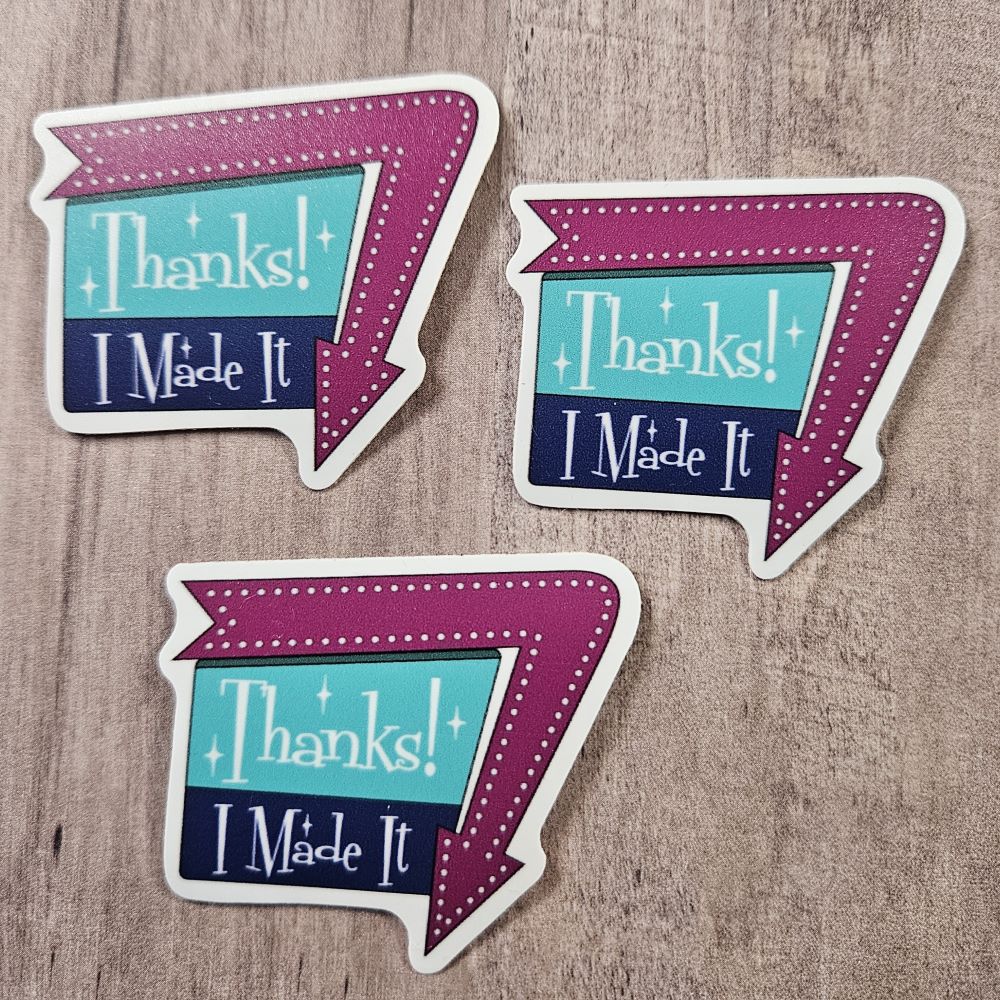 three stickers that say "Thanks! I Made It" in a 1960 sign style with arrow around one edge pointing down. Arrow is a warm purple, and the sign is aqua and dark blue with white writing 
