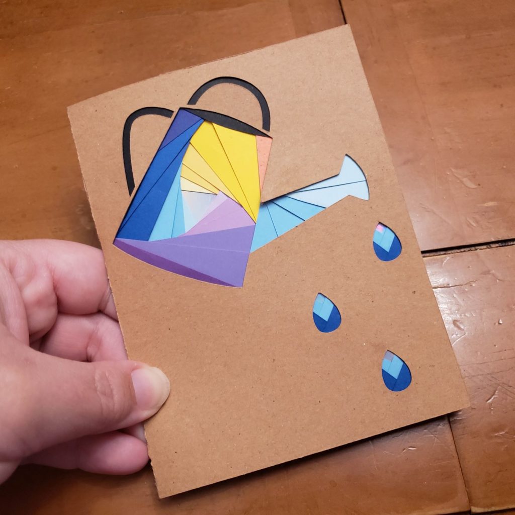 Card with watering can on the front. Can outline is filled with swirled papers that come to a metallic center. Using Iris Paper Folding