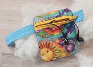 small zippered pouch made out a fabric with suns on it. It has a blue elastic strap and ear buds sticking out of it. 